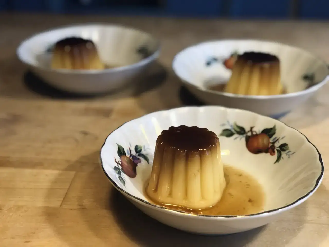 Tre krämiga creme caramel i vackra skålar med fruktmotiv. En härlig dessert som väntar.