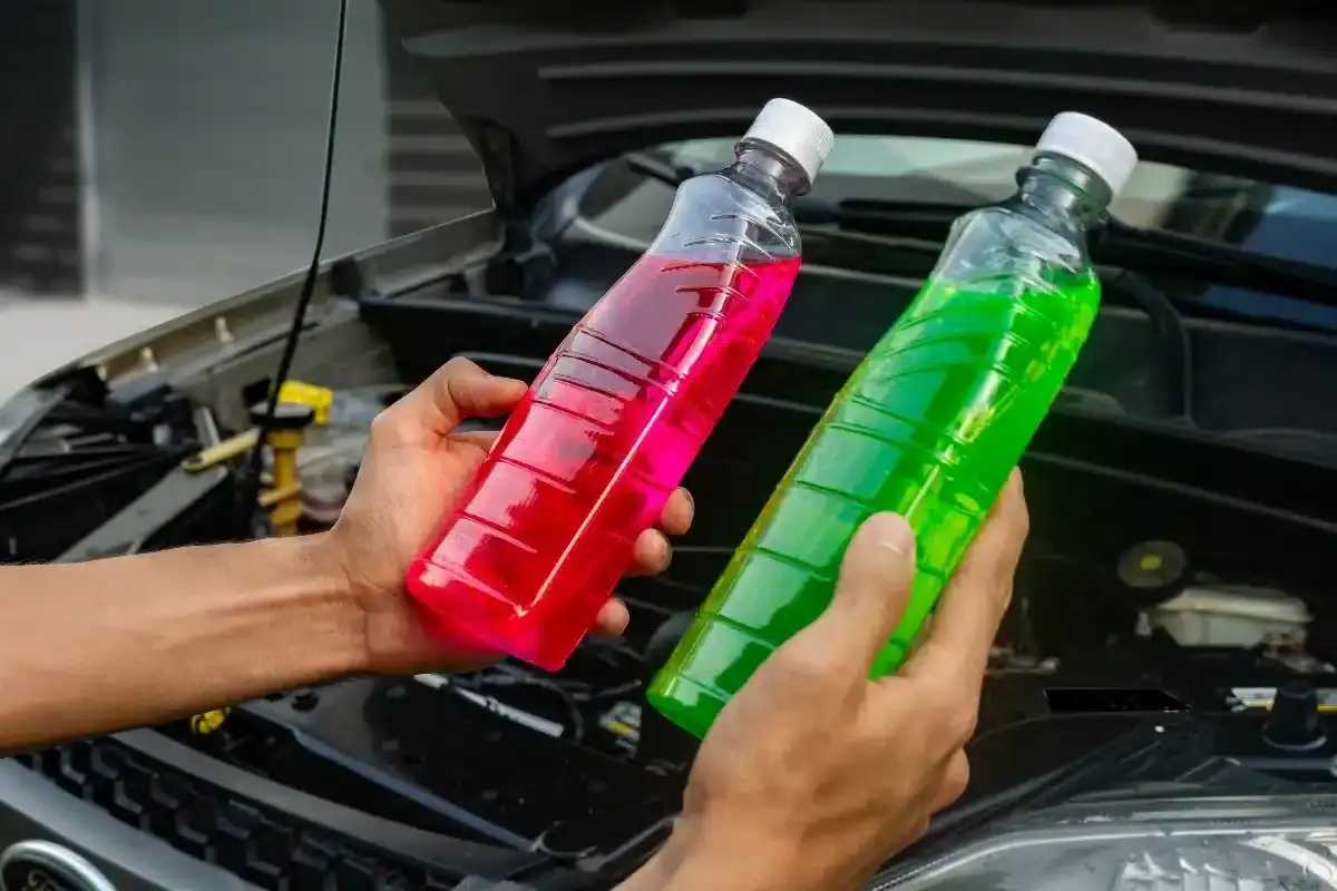 Deux mains tiennent des bouteilles de liquide de refroidissement coloré, rose et vert. Quel liquide de refroidissement choisir pour votre voiture ?