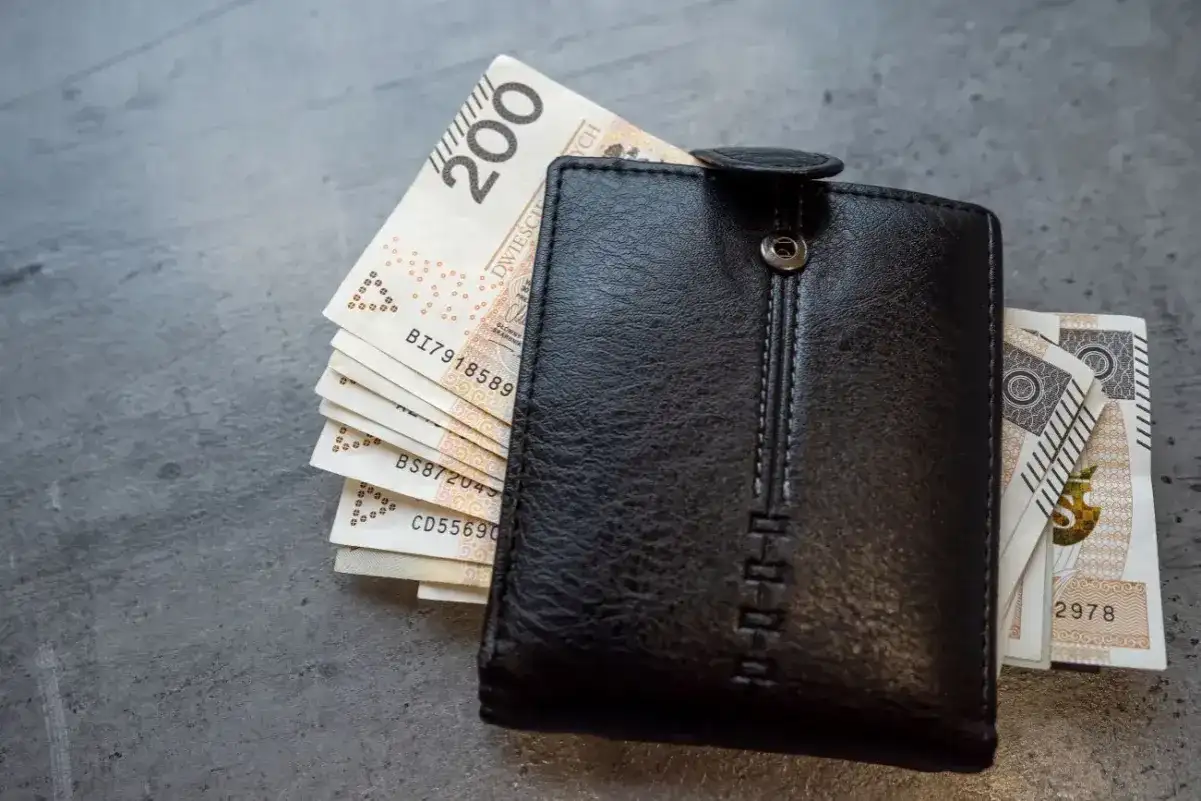 Czarny portfel z polskimi banknotami. Zastanawiasz się, jak obliczyć chorobowe w ciąży? Finanse przyszłej mamy.