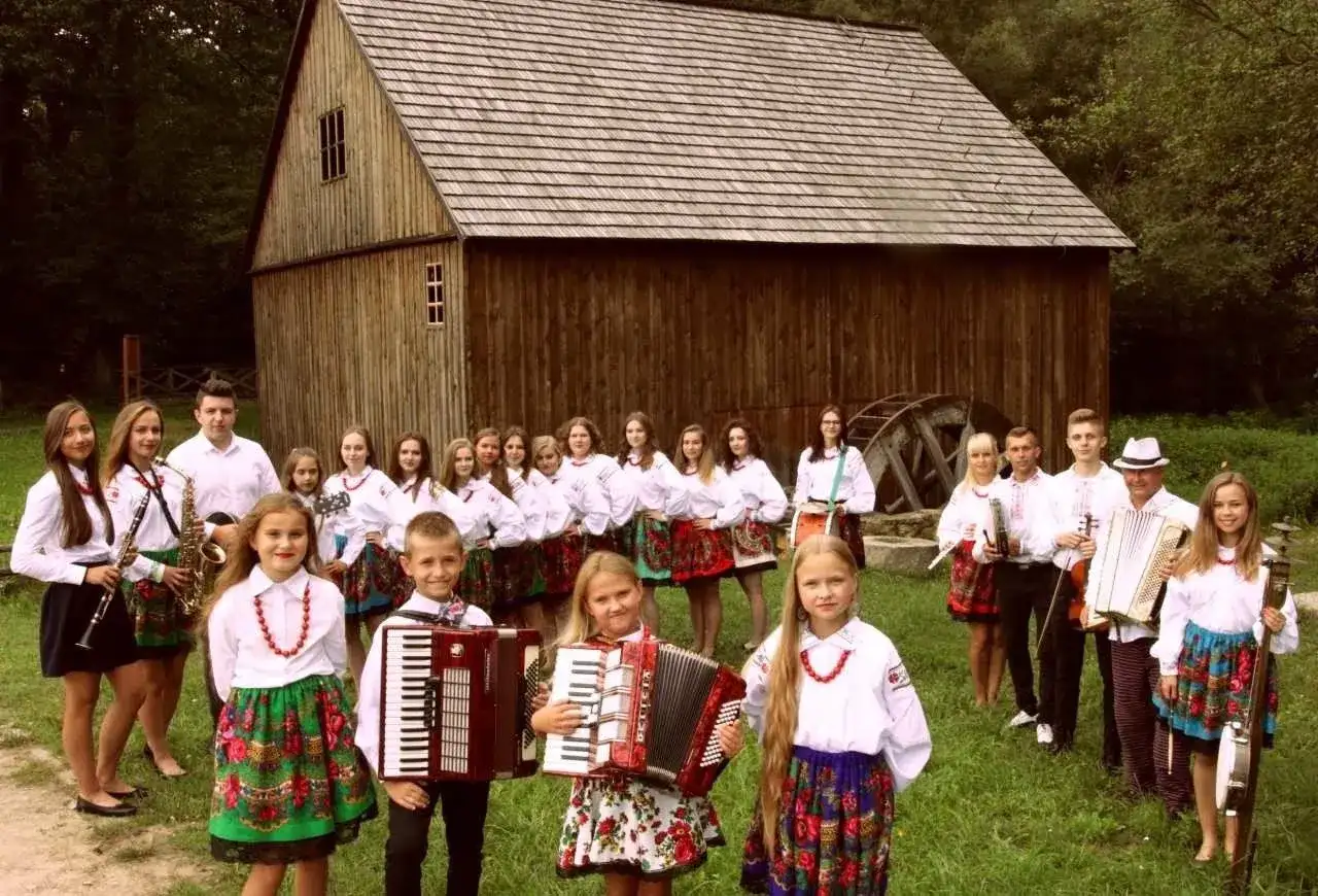 Guzowianki w ludowych strojach, z akordeonami i instrumentami, gotowe do występu.