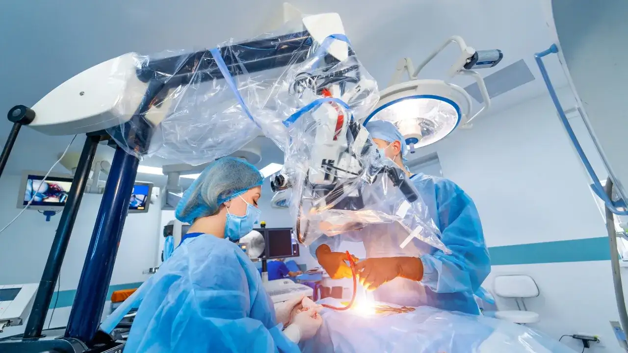 Chirurdzy w sterylnych strojach prowadzą skomplikowaną operację neurochirurgiczną pod mikroskopem.