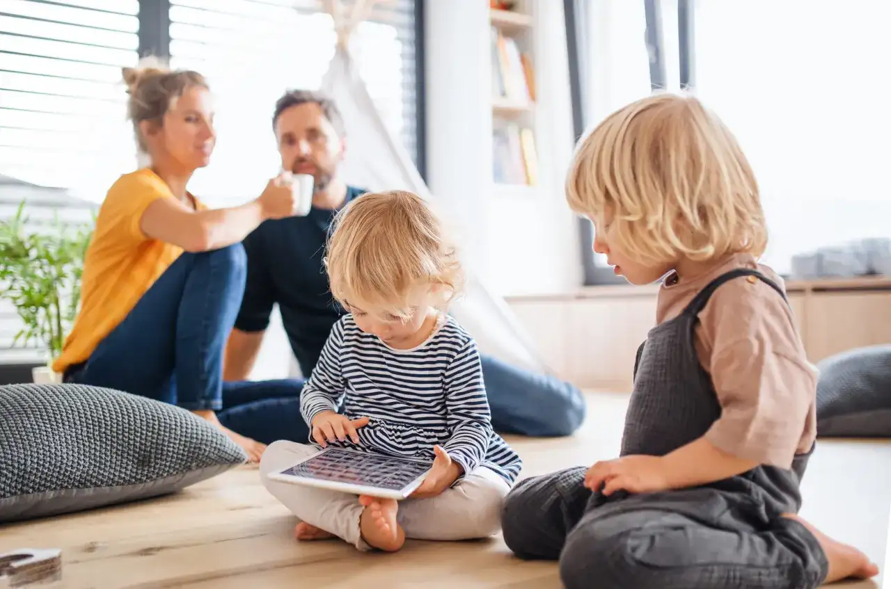 Rozpieszczone dziecko pochłonięte tabletem, podczas gdy rodzice w tle piją kawę.