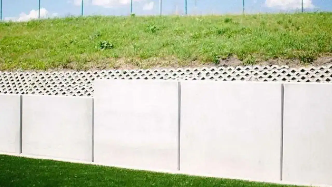 Nowy mur oporowy odległość od granicy działki. Betonowe płyty i ażurowa warstwa pod zielonym nasypem.