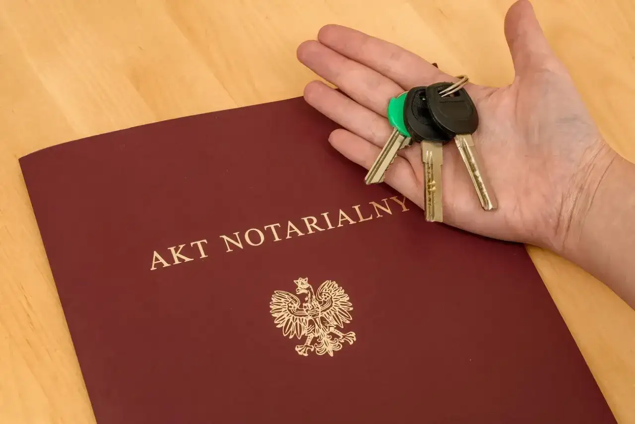 Akt notarialny i klucze w dłoni. Komparycja dokumentów i symbolu własności.