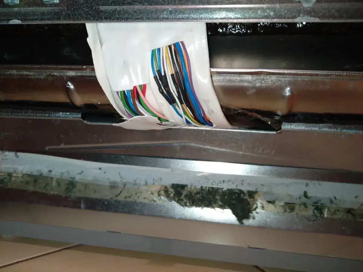 Zmywarka Beko błąd E02: widoczne uszkodzone przewody i brud pod metalową osłoną.