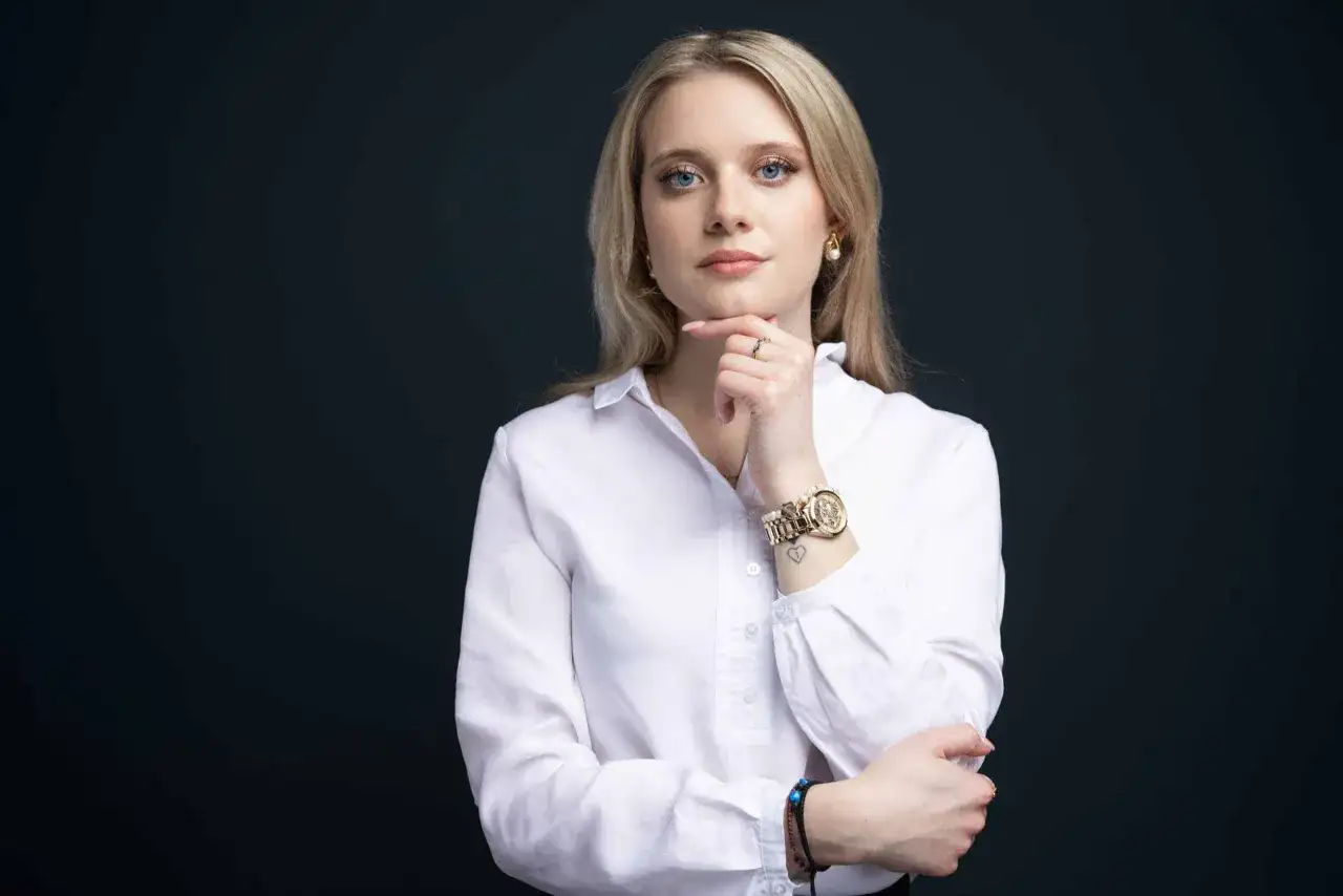 Kobieta w białej koszuli, z ręką na podbródku, pokazuje, jak zrobić zdjęcie biznesowe w domu.