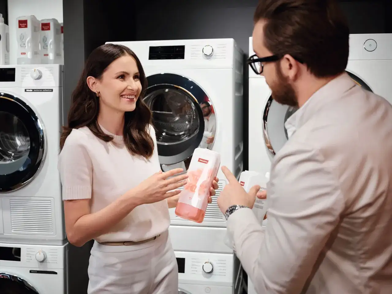 Kobieta i mężczyzna rozmawiają o produktach do prania Miele, stojąc przed nowoczesnymi pralkami.