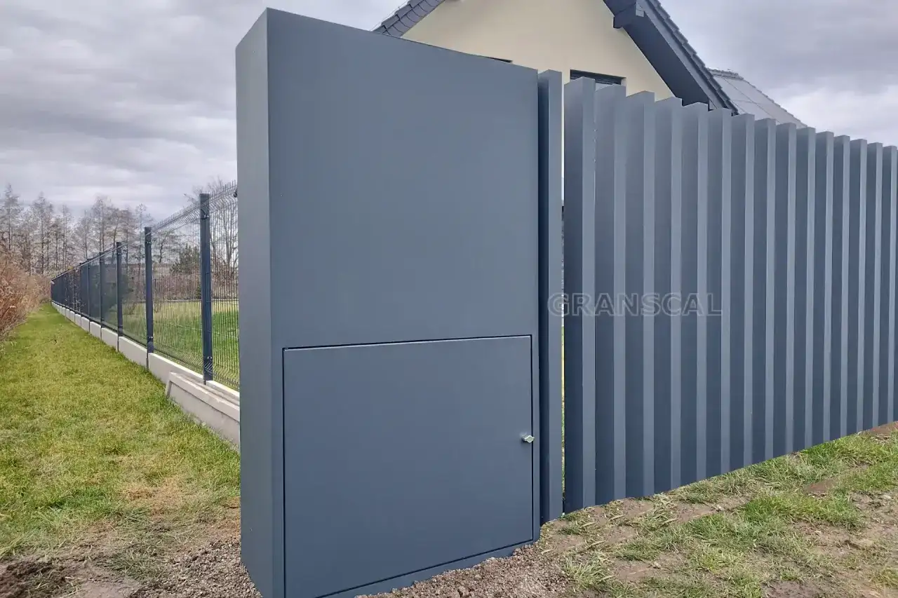 Nowoczesne ogrodzenie z pionowych paneli i słupka z ukrytą skrzynką elektryczną. Czy skrzynka elektryczna musi być w ogrodzeniu? Tutaj jest dyskretnie wkomponowana.