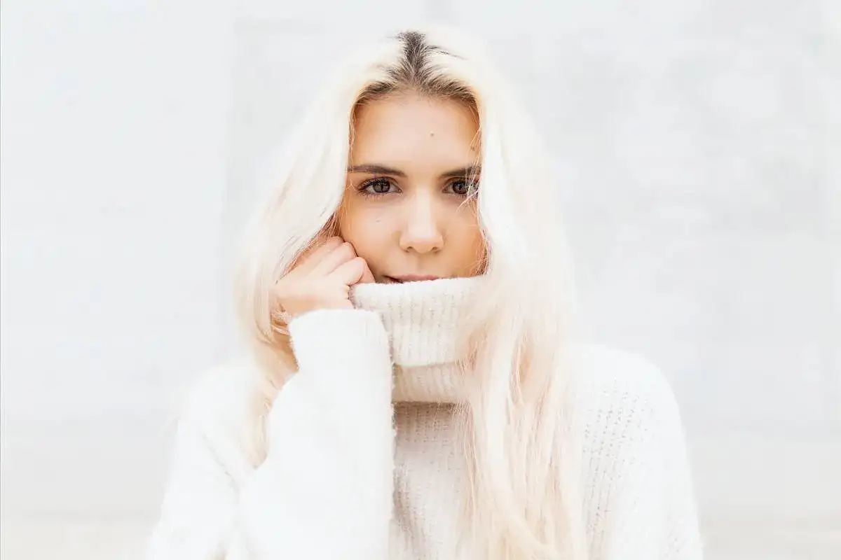 Blondynka w białym golfie, z włosami opadającymi na ramiona, wygląda jak uosobienie stylu vanilla girl.