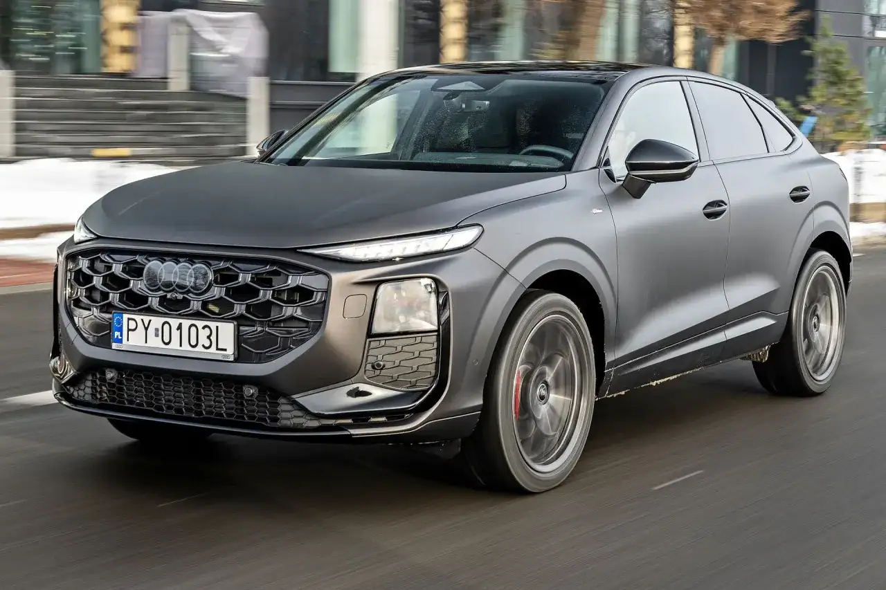 Nowe Audi Q3 w matowym, grafitowym kolorze sunie po drodze, prezentując swój sportowy charakter i nowoczesny design.