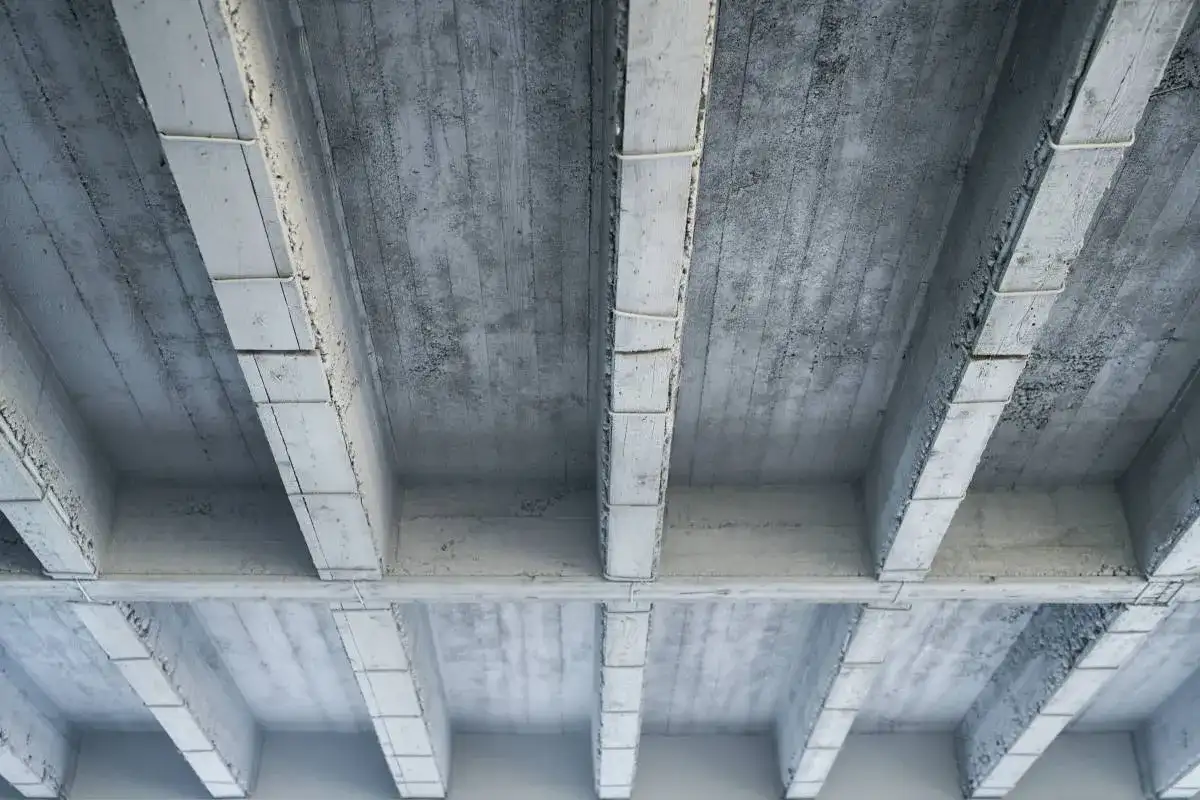 Widok od dołu na betonowy strop z belkami. Obliczenia obciążenia stropu żelbetowego na m2 są kluczowe dla bezpieczeństwa konstrukcji.