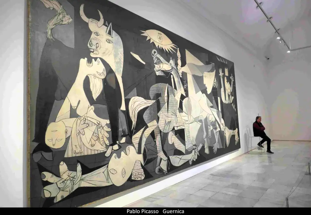 Pablo Picasso najsłynniejsze obrazy: "Guernica" w muzeum, z człowiekiem siedzącym na krześle i kontemplującym dzieło.