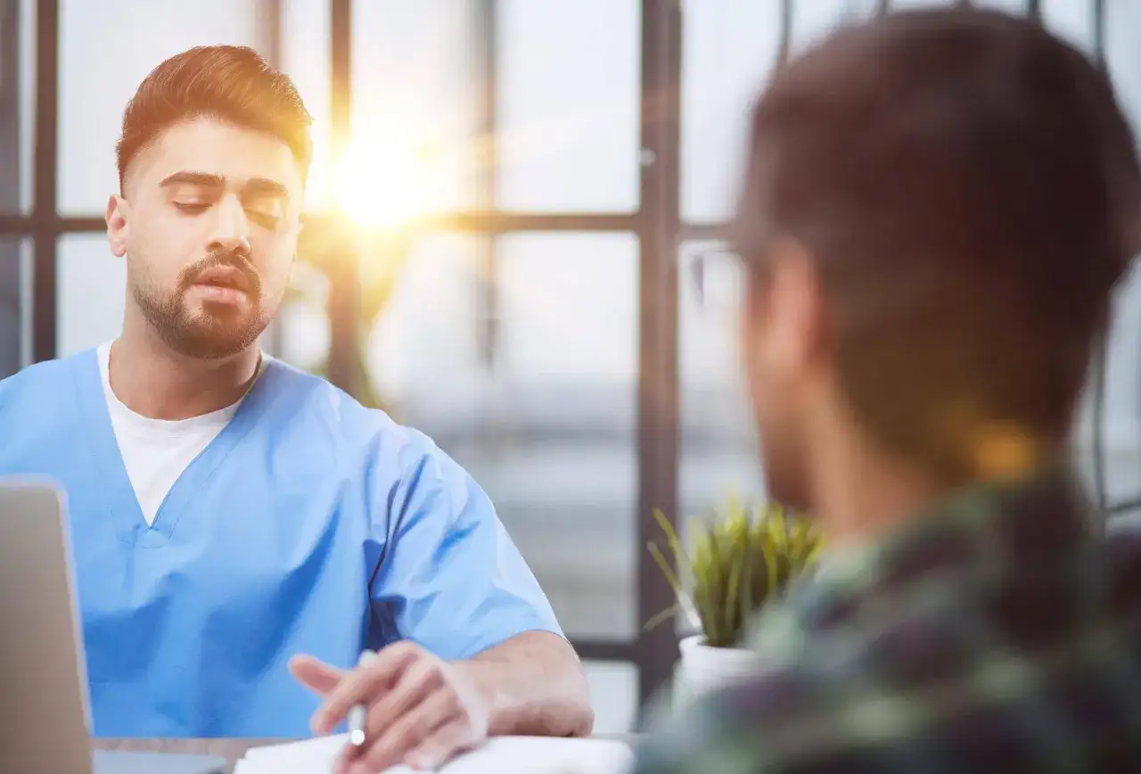 Lekarz w niebieskiej koszuli rozmawia z pacjentem. Czy trzeba mieć skierowanie do psychiatry? Zapytaj lekarza.