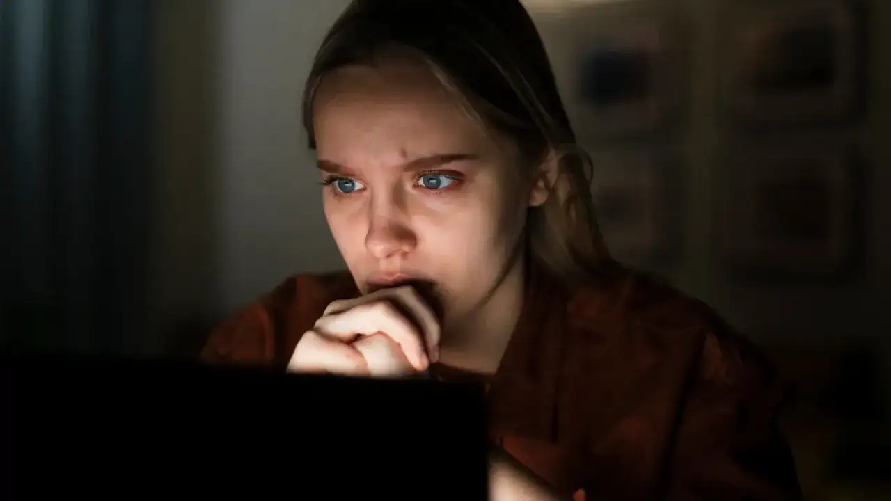 Przerażona dziewczyna wpatruje się w ekran, czując się jak ofiara stalkingu.
