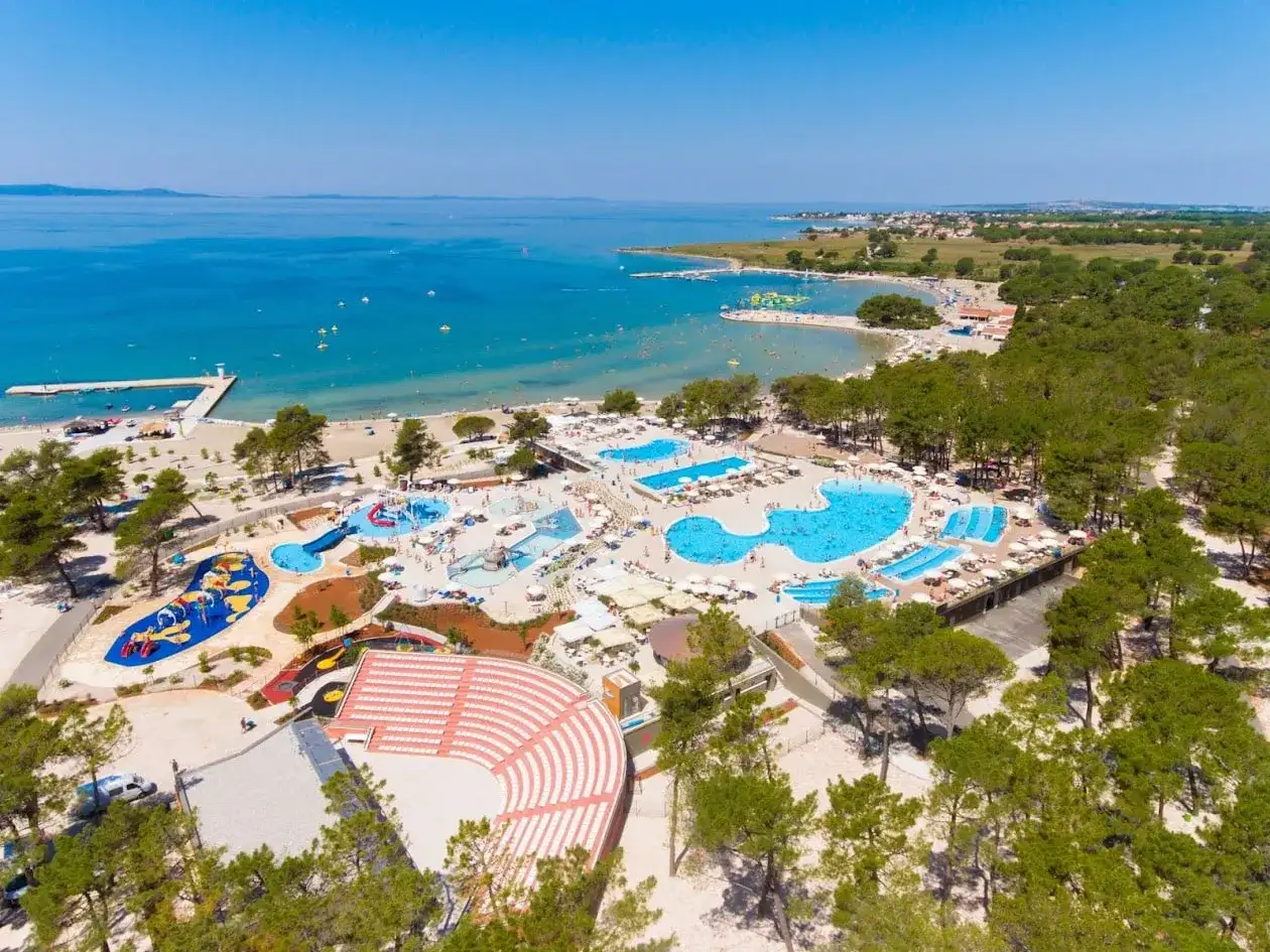 Widok z lotu ptaka na kompleks basenów i plażę z turystami w słoneczny dzień.