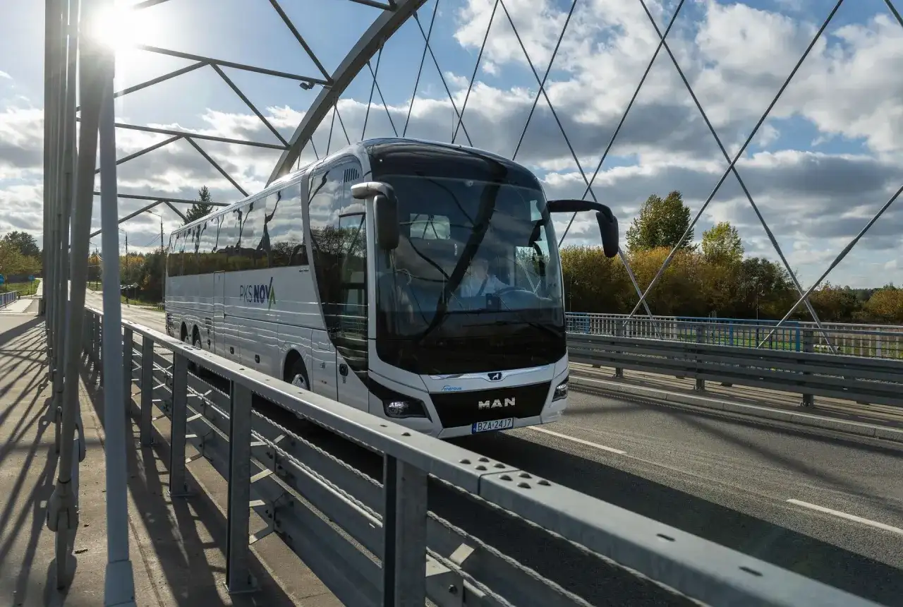 Autobus PKS NOVA na moście, podróżujący z Grajewa do Augustowa. Słoneczny dzień, chmury na niebie.