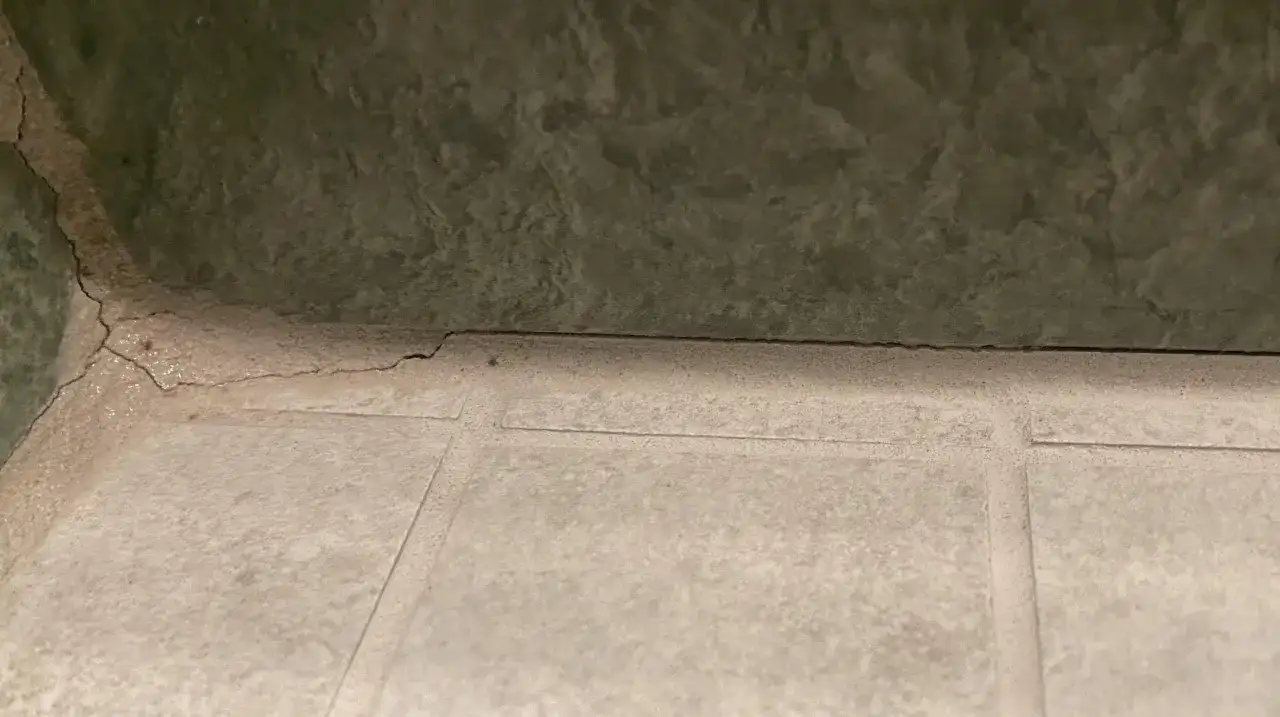 Pęknięta, biała masa między płytkami sugeruje, że szukamy co zamiast fugi. Zielona ściana nad nią.