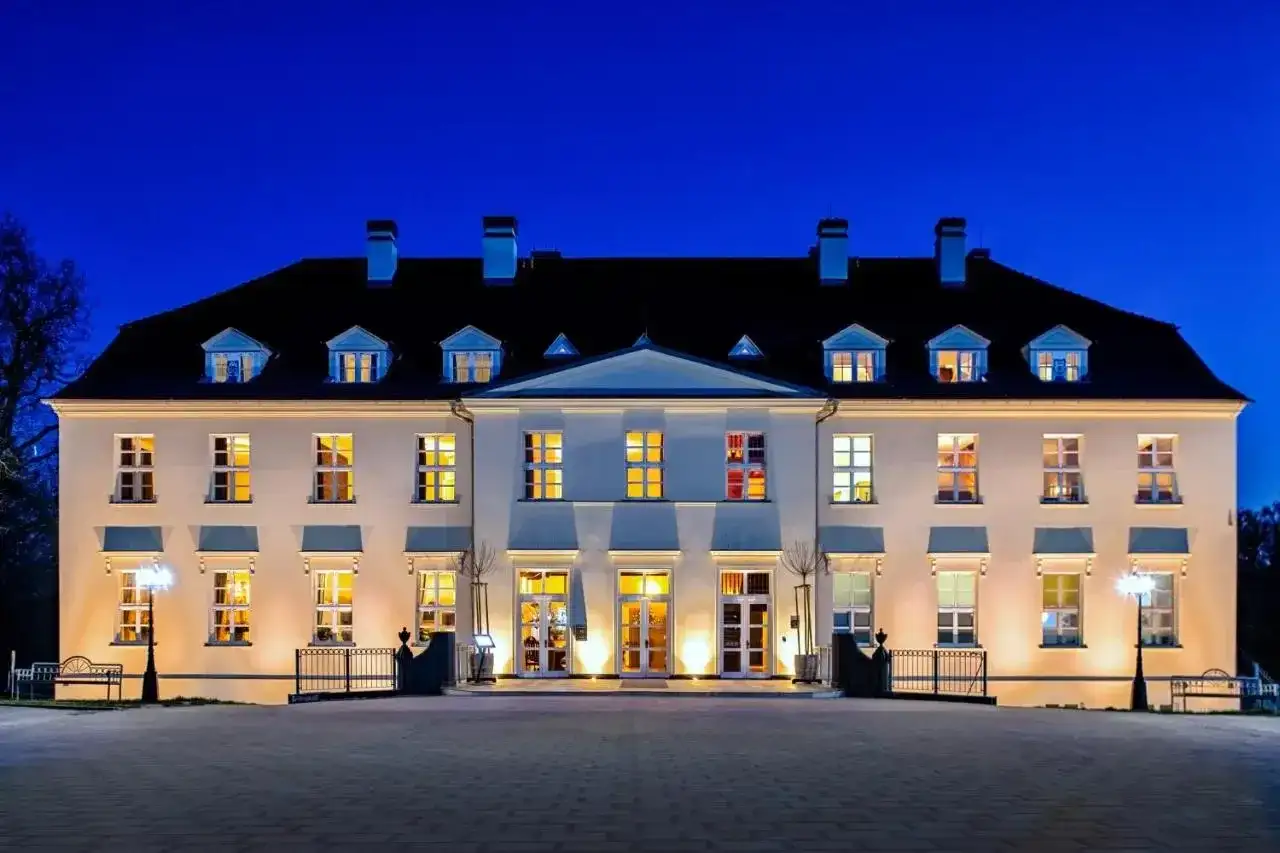 Beleuchtetes Schloss mit vielen Fenstern bei Nacht vor blauem Himmel.