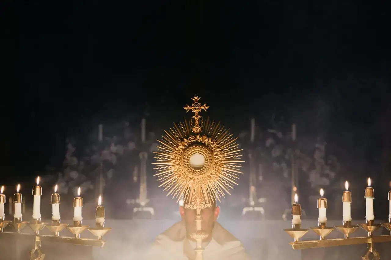 Złota monstrancja z hostią, otoczona płonącymi świecami, symbolizuje obecność Chrystusa. To obraz nawiązujący do 7 sakramentów świętych.