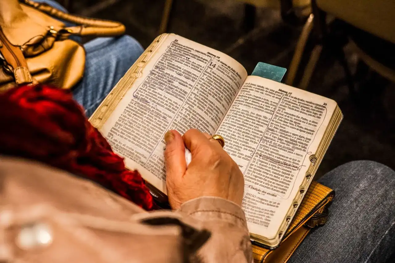 Osoba czyta Biblię, skupiając się na psalm 9. W tle widać torebkę i fragmenty ubrania.