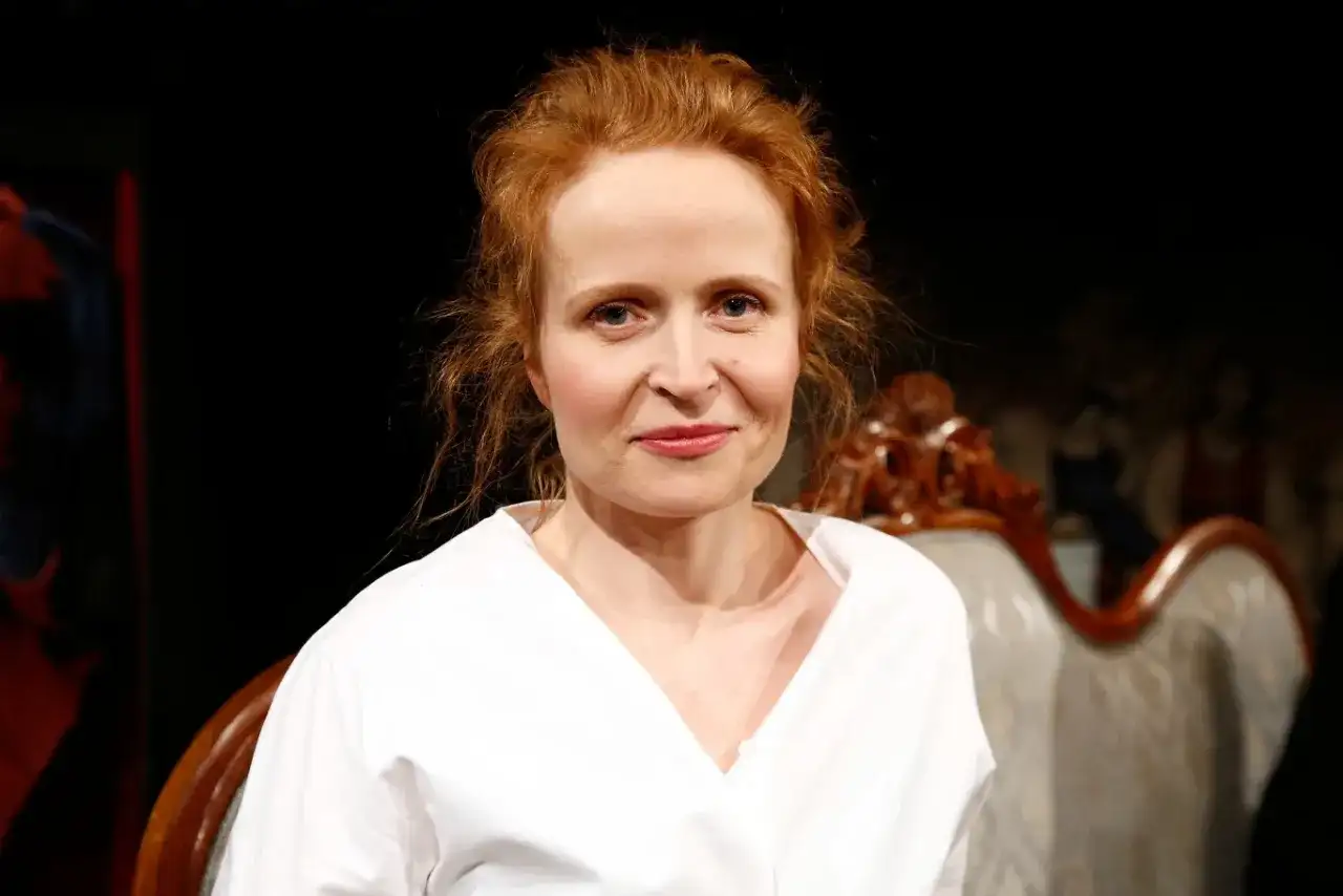 Dominika Kluźniak w białej koszuli, aktorka znana z filmów, seriali i programów, uśmiecha się lekko.