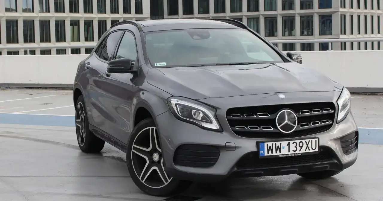 Szary Mercedes GLA 220 z polskimi tablicami rejestracyjnymi stoi na parkingu przed nowoczesnym budynkiem.