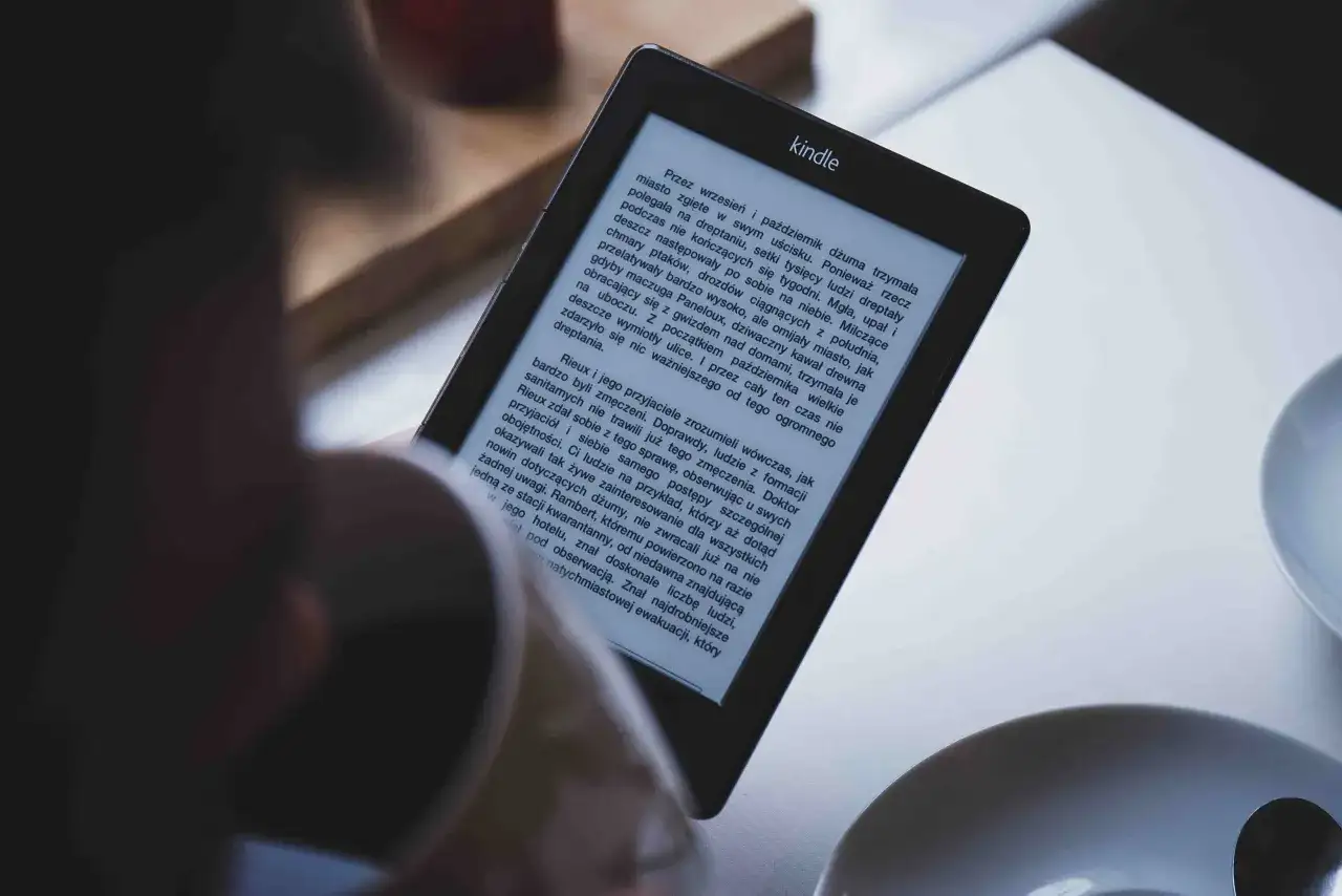 Osoba czyta książkę w formacie kindle. Na ekranie widoczny jest tekst powieści.