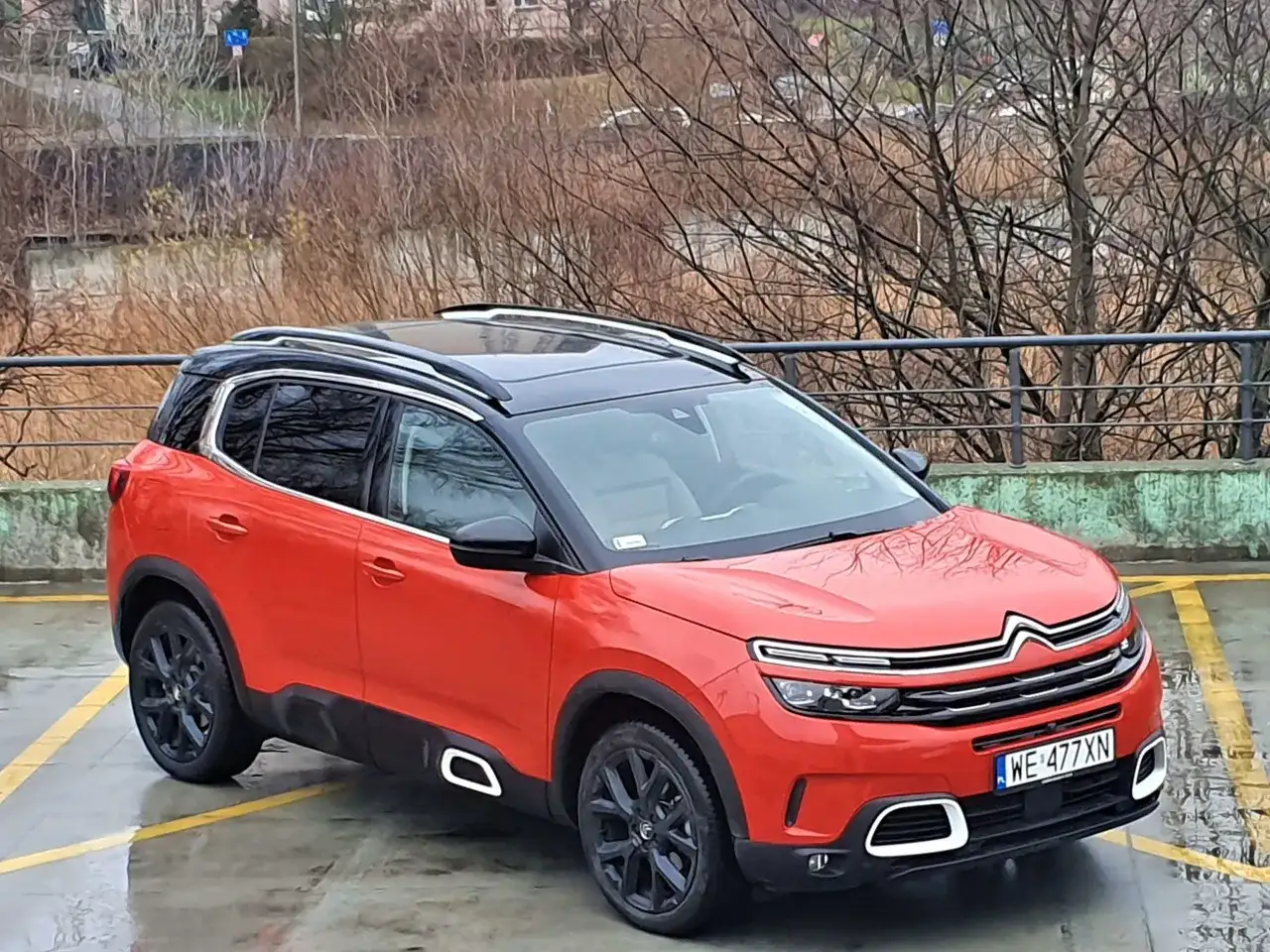 Pomarańczowy Citroen C5 Aircross z czarnym dachem stoi na mokrym parkingu.