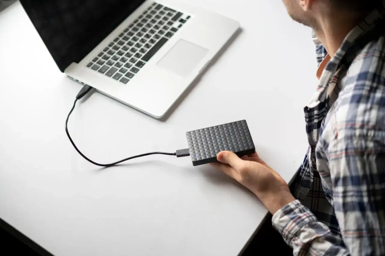 Mężczyzna podłącza dysk zewnętrzny do laptopa, przygotowując się do użycia narzędzia diskpart.