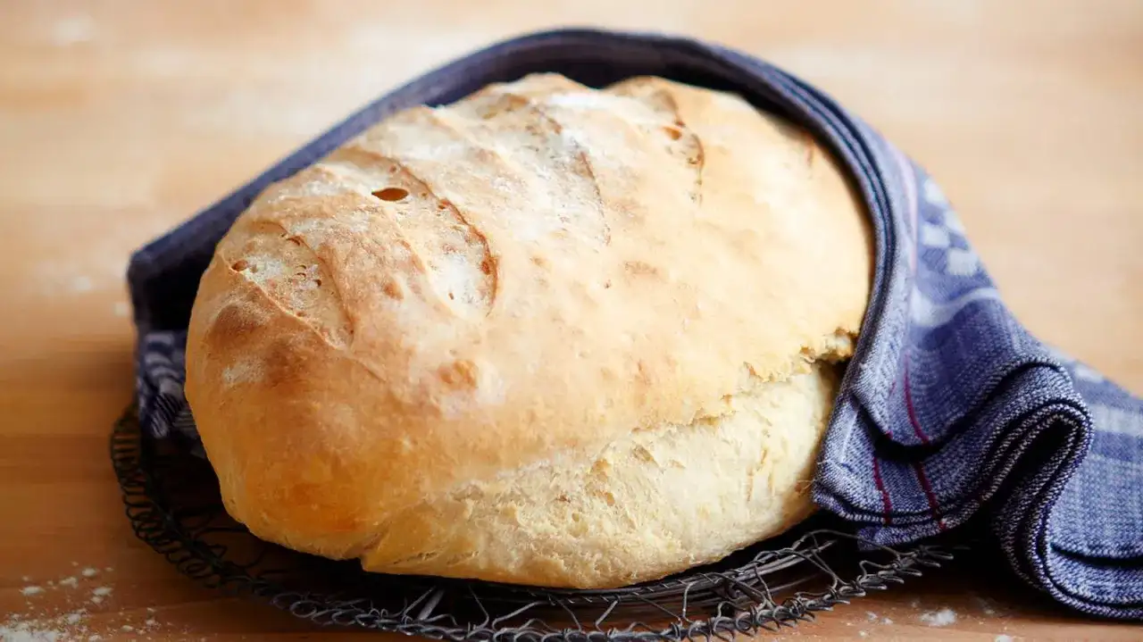 Frisch gebackenes Brot, das nach dem **Brot selber backen** auf einem Gitter abkühlt. Ein blau-weißes Tuch umhüllt es.