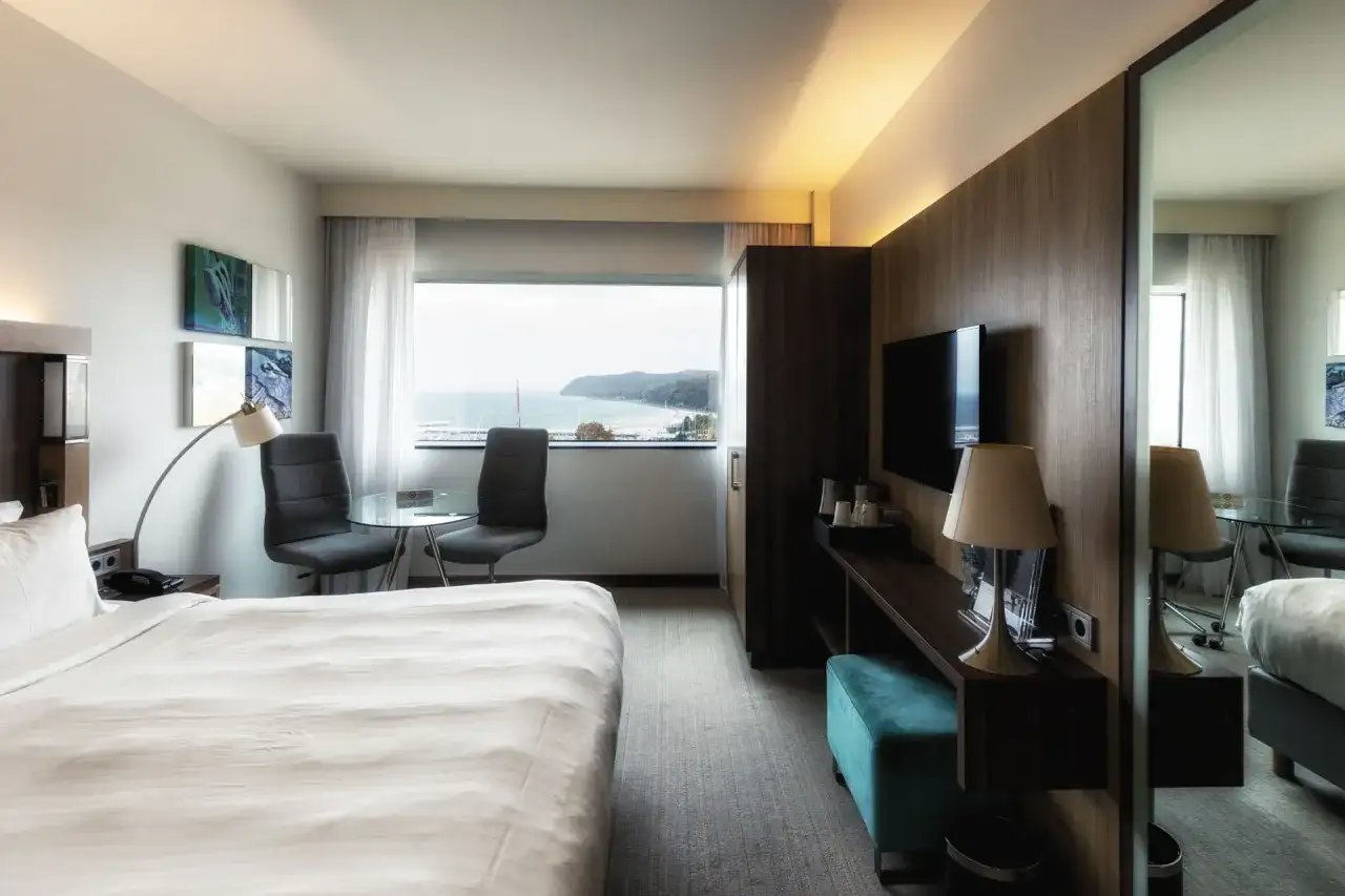 Pokój w hotelu Marriott Gdynia z widokiem na morze. Wygodne łóżko, stolik z krzesłami i telewizor.