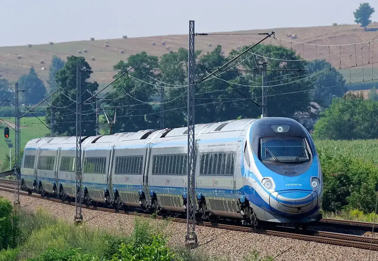 Szybki pociąg Pendolino mknie po torach, pokonując **drogę do Gdańska**. W tle zielone pola i drzewa.