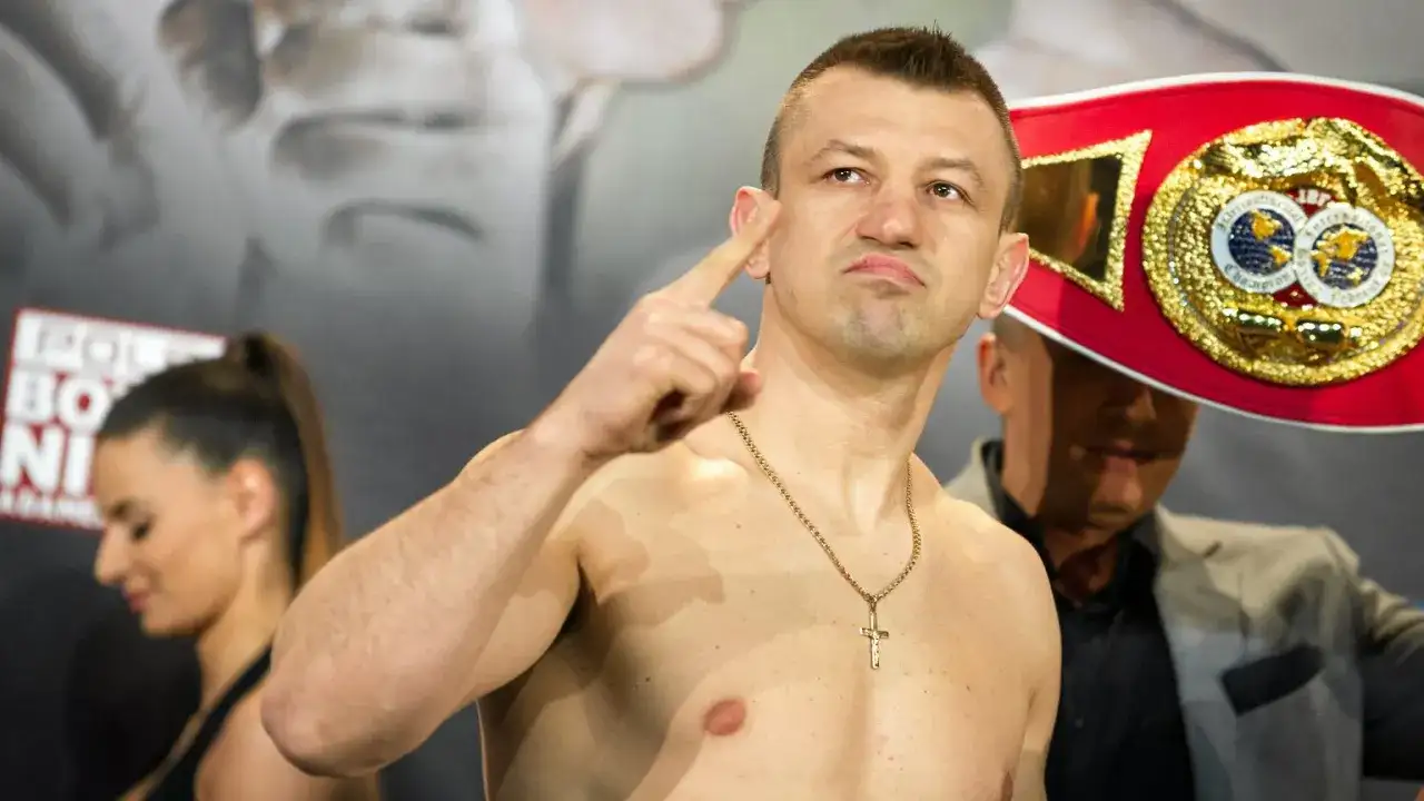 Adamek, znany z kariery bokserskiej, pokazuje swój pas mistrzowski, gotowy na walkę w świecie fame MMA.