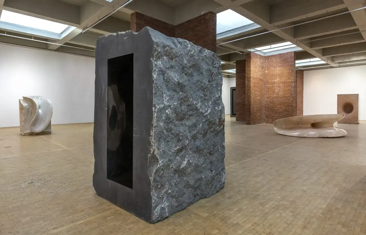 Kamienna rzeźba z czarnym wnętrzem, część wystawy Anish Kapoor w Orońsku. W tle inne dzieła sztuki.