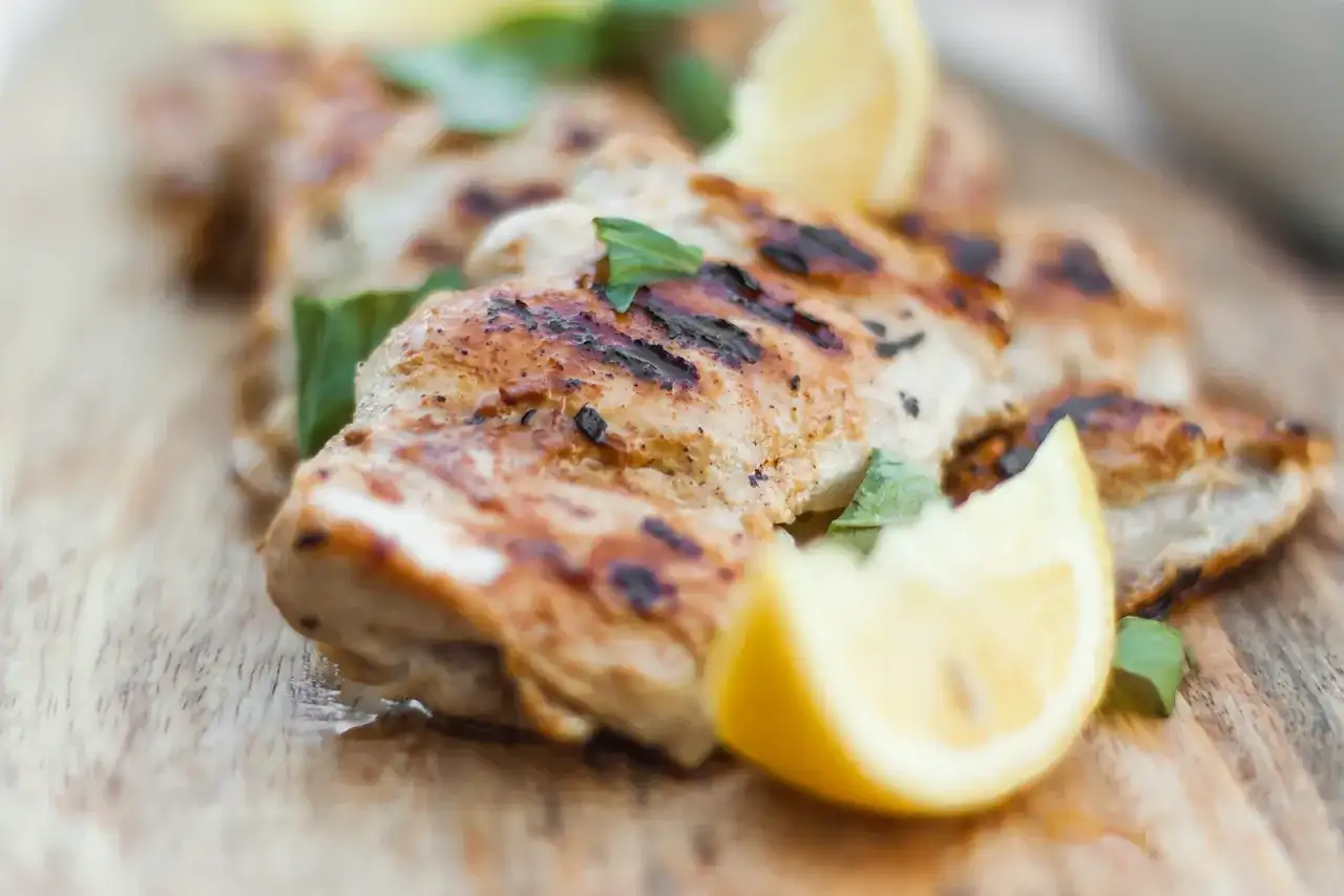 Grillowany kurczak w jogurcie, podany z cytryną i ziołami na drewnianej desce.