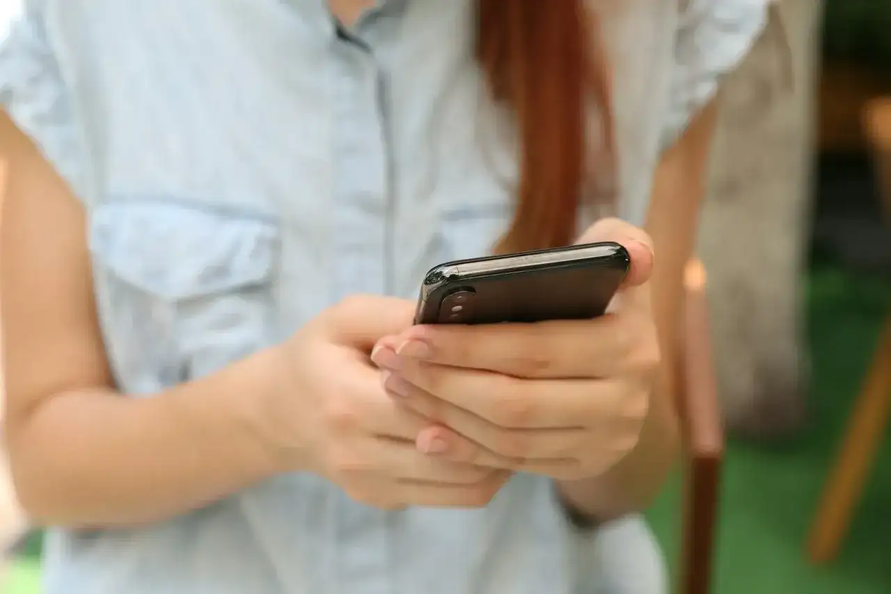 Kobieta z rudymi włosami trzyma smartfon, szukając informacji, gdzie sprawdzić L4.
