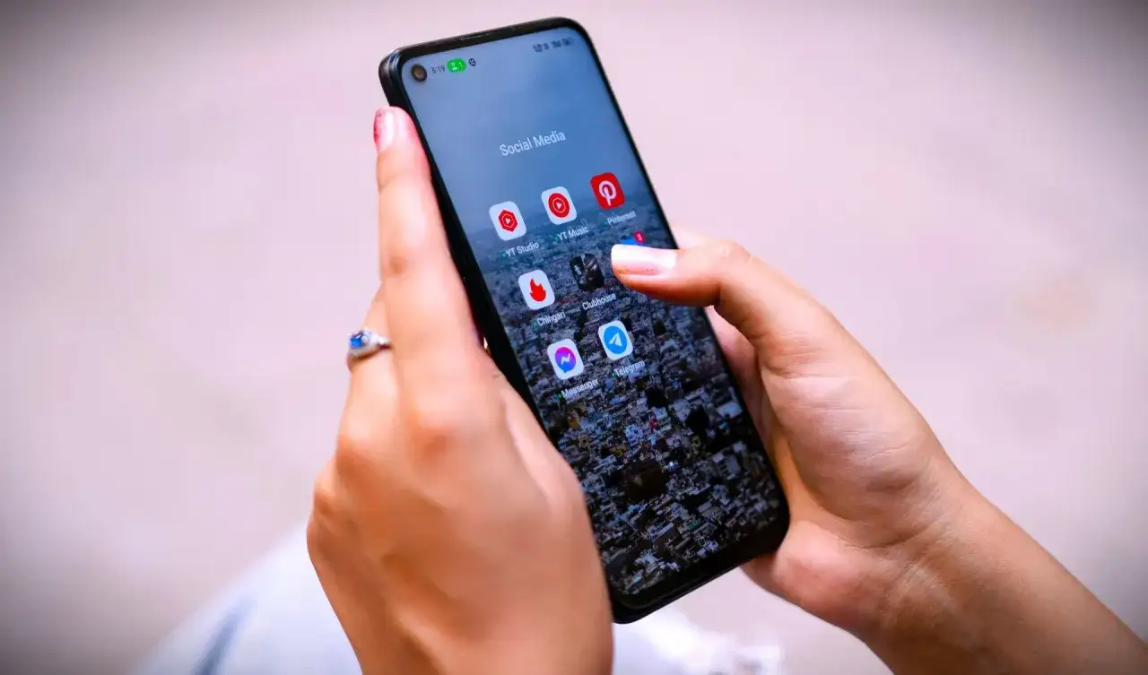 Dłonie trzymają telefon z ikonami aplikacji społecznościowych. Zastanawiasz się, jak trwale usunąć wiadomości z Messengera?