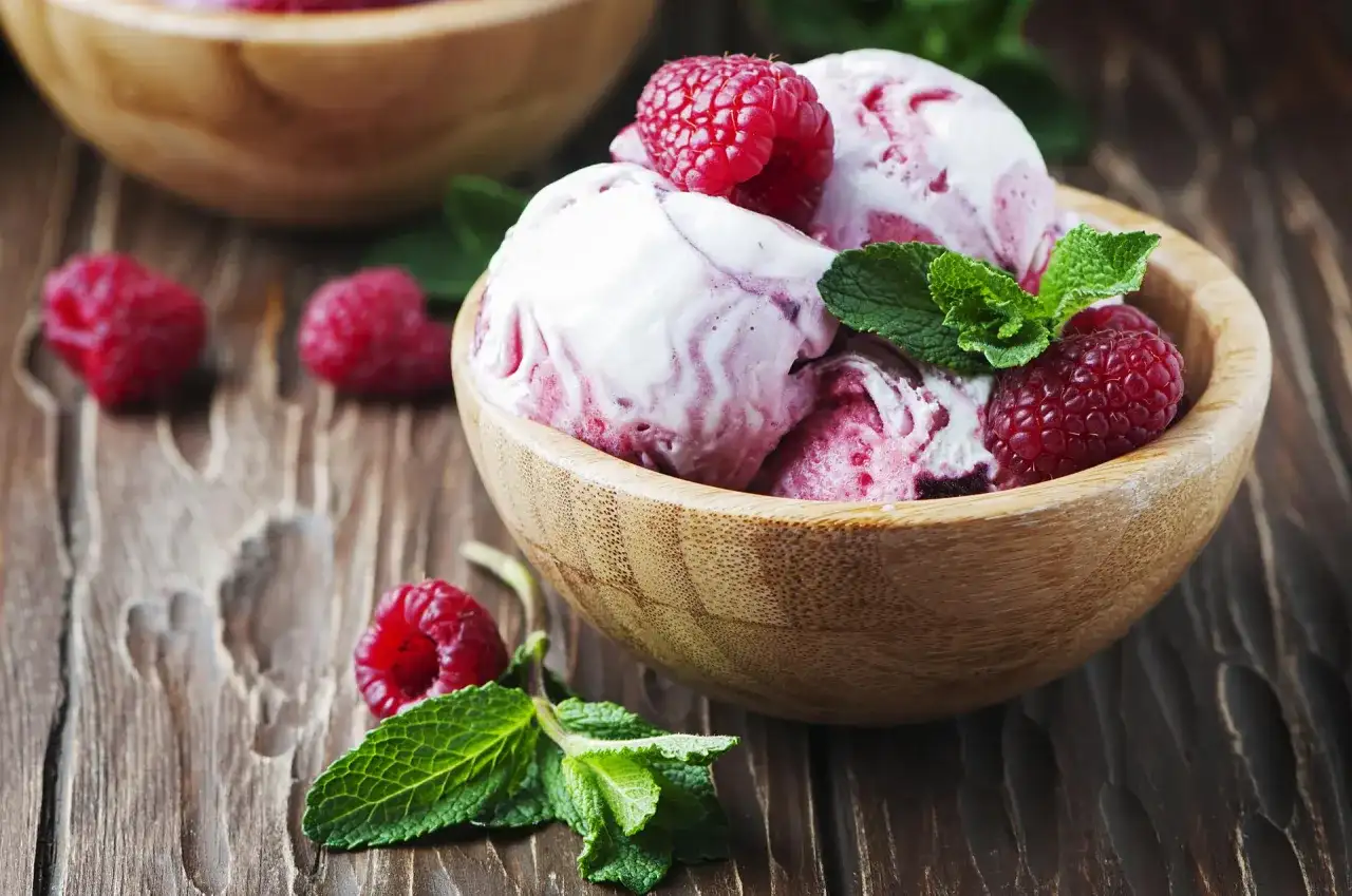 Pyszny sorbet malinowy w drewnianej miseczce, ozdobiony świeżymi malinami i miętą. Idealny deser, jak zrobić sorbet malinowy.
