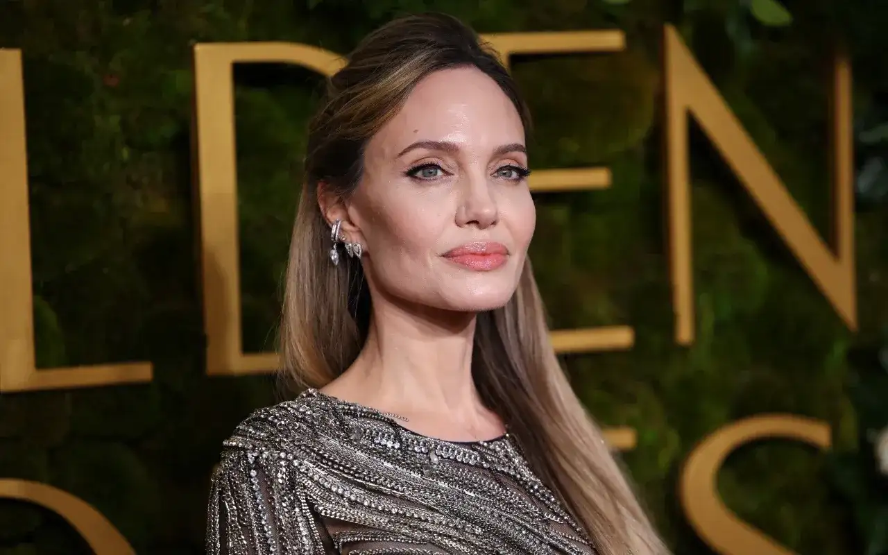 Angelina Jolie, jedna z najbardziej znanych aktorek Hollywood, w błyszczącej kreacji na tle złotych liter.