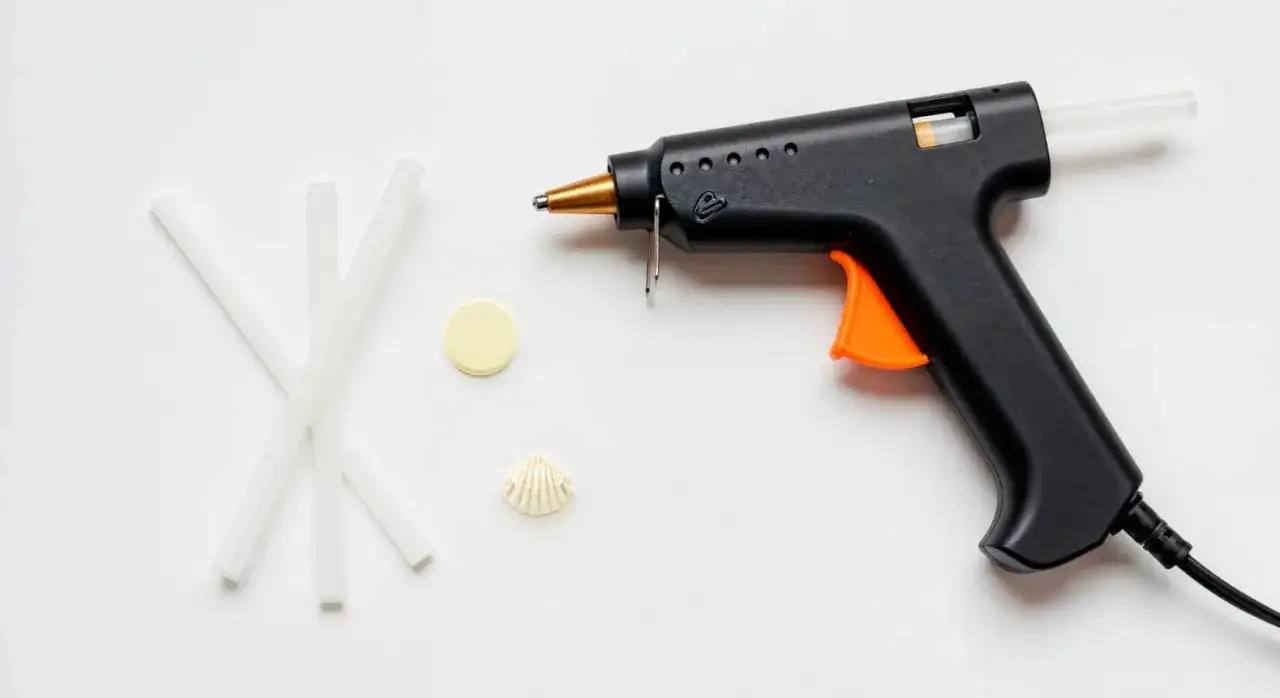 Czarny pistolet do kleju na gorąco z pomarańczowym spustem i kilkoma pałeczkami kleju obok. Dowiedz się, jak włożyć klej do pistoletu.