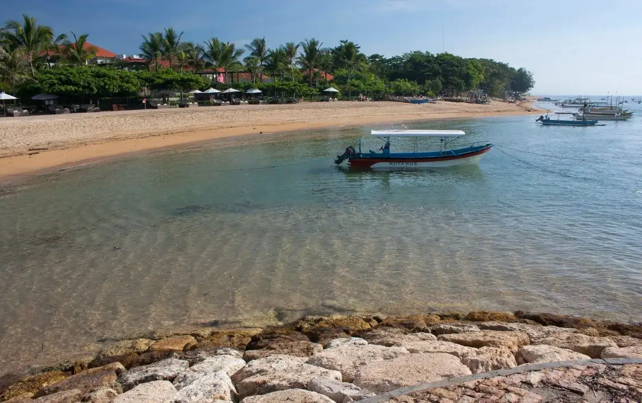 Spokojna plaża w Sanur z łodzią "Water Walk" kołyszącą się na turkusowej wodzie.