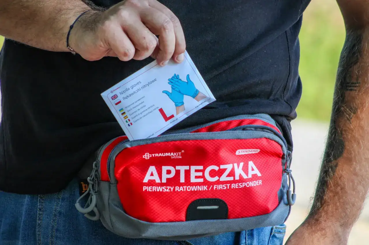 Dłoń wyjmuje z apteczki "Pierwszy ratownik" opakowanie rękawiczek nitrylowych.