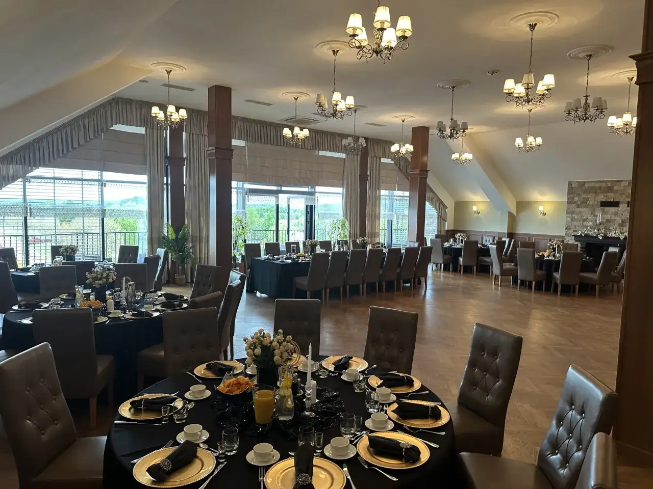 Elegancka sala bankietowa w ośrodku jeździeckim Lando, przygotowana na przyjęcie. Stoły nakryte czarnymi obrusami, złote talerze i eleganckie krzesła.