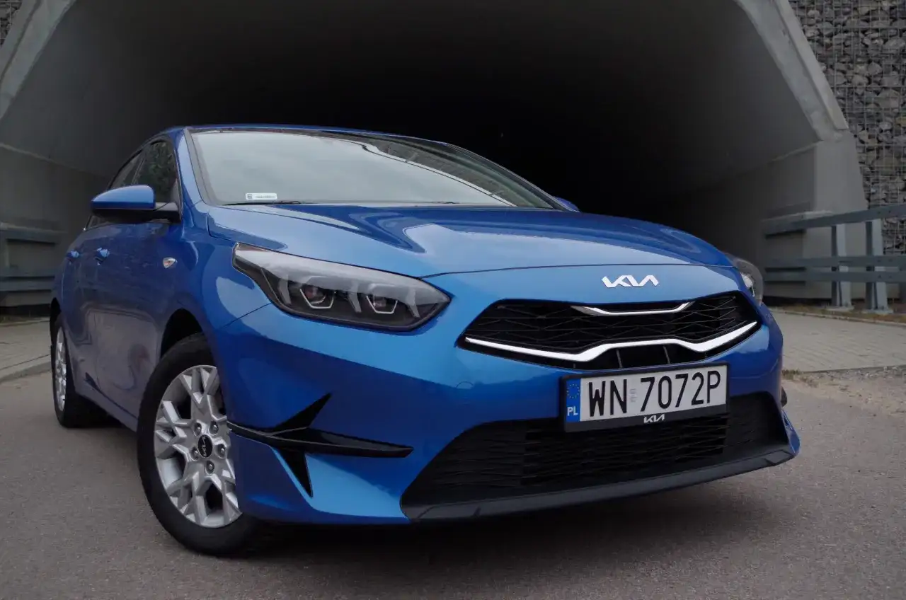 Niebieska Kia Ceed 1.5 T-GDI z nowoczesnymi światłami i grillem, zaparkowana przy betonowym tunelu.