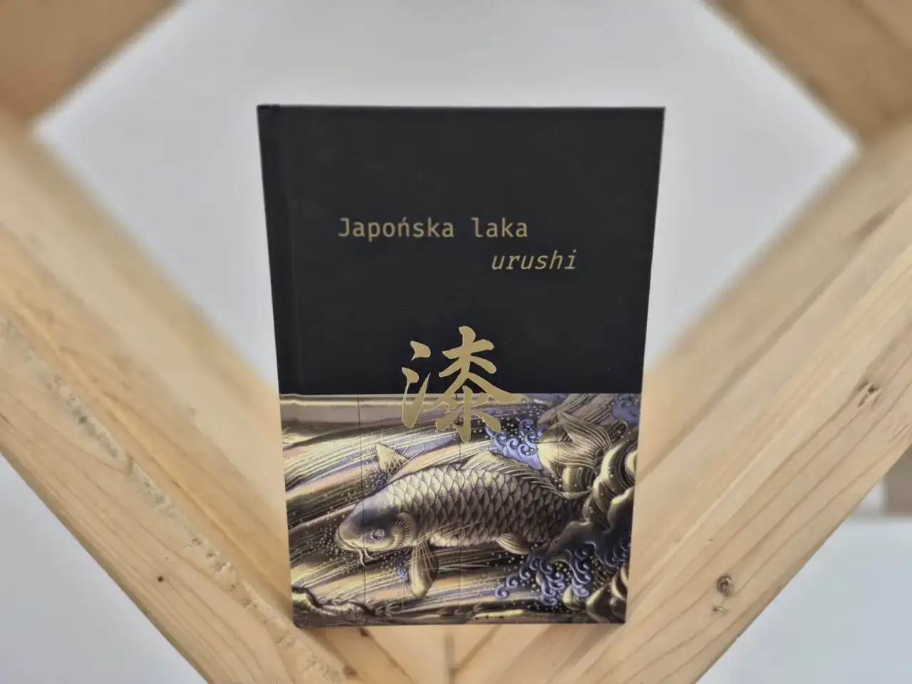 Okładka książki "Japońska laka urushi" z motywem złotej ryby koi i japońskiego znaku.