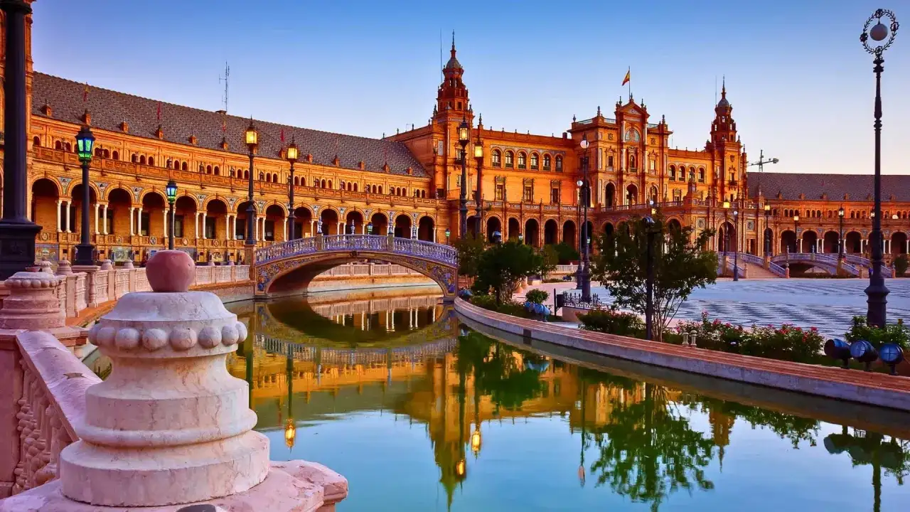 Plaza de España en Sevilla, una de las ciudades que ver en España. Reflejos dorados en el canal y un puente ornamentado.