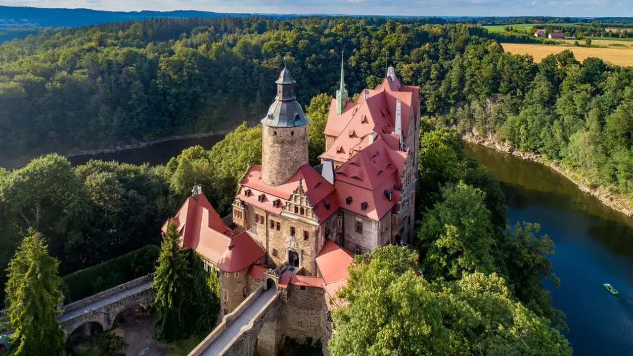 Zamek Czocha, malowniczo położony nad rzeką, otoczony bujną zielenią.