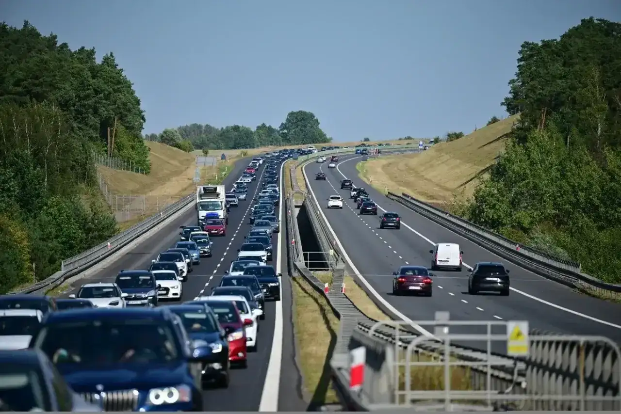 Długi korek samochodów na autostradzie A6. Wiele pojazdów stoi w powolnym ruchu, otoczonych zielenią drzew.