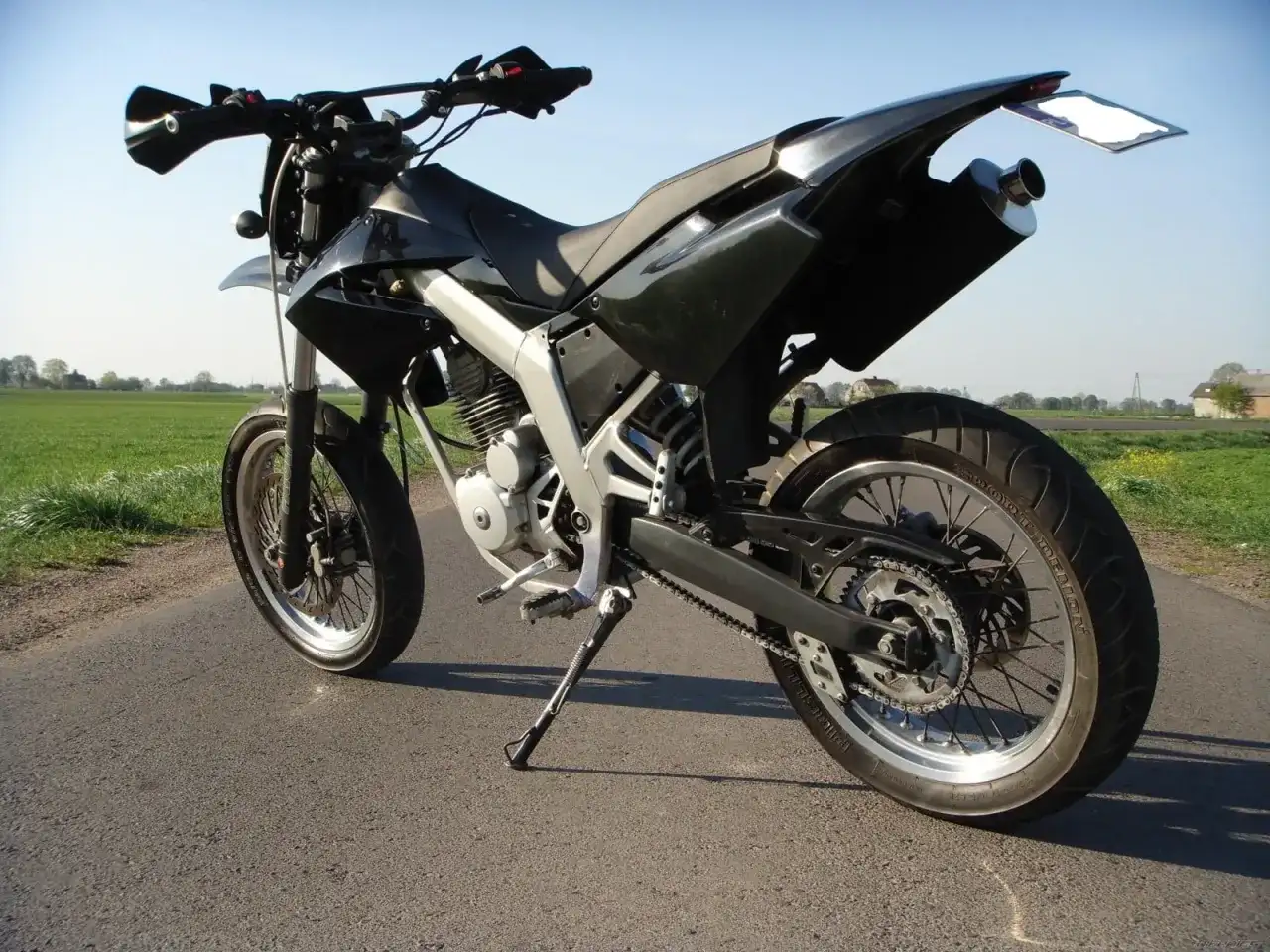 Czarny motocykl typu supermoto, gotowy do jazdy po wiejskich drogach. Senda czeka na przygodę.