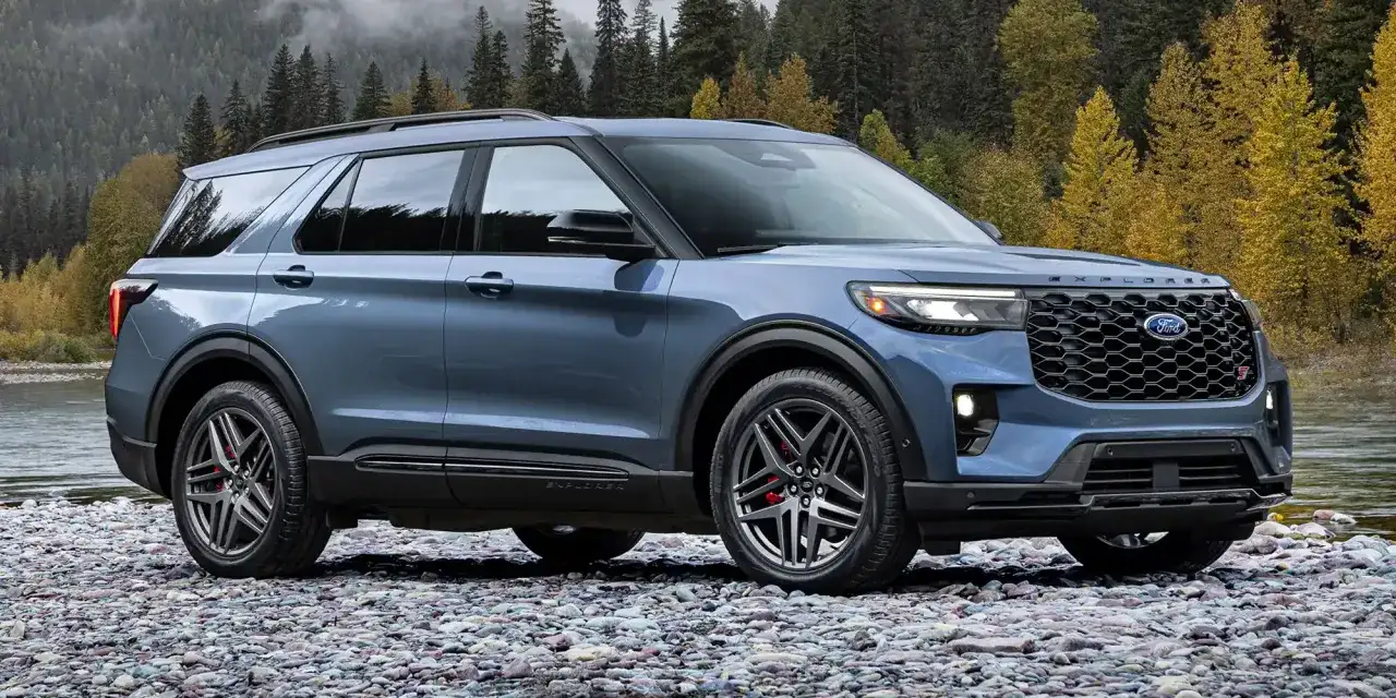 Niebieski Ford Explorer ST na kamienistej plaży, z jesiennym lasem w tle.